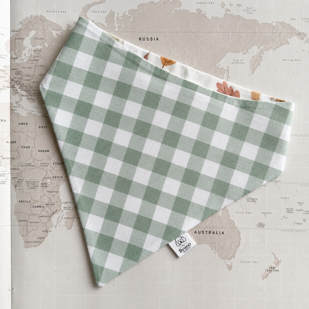 A green and white gingham check bandana with a small white sewn label, laid flat on a vintage-style world map background.