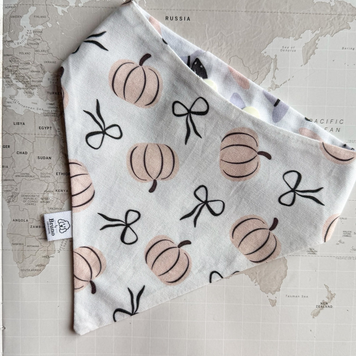 White cotton dog bandana with pastel orange pumpkins and black ribbons.