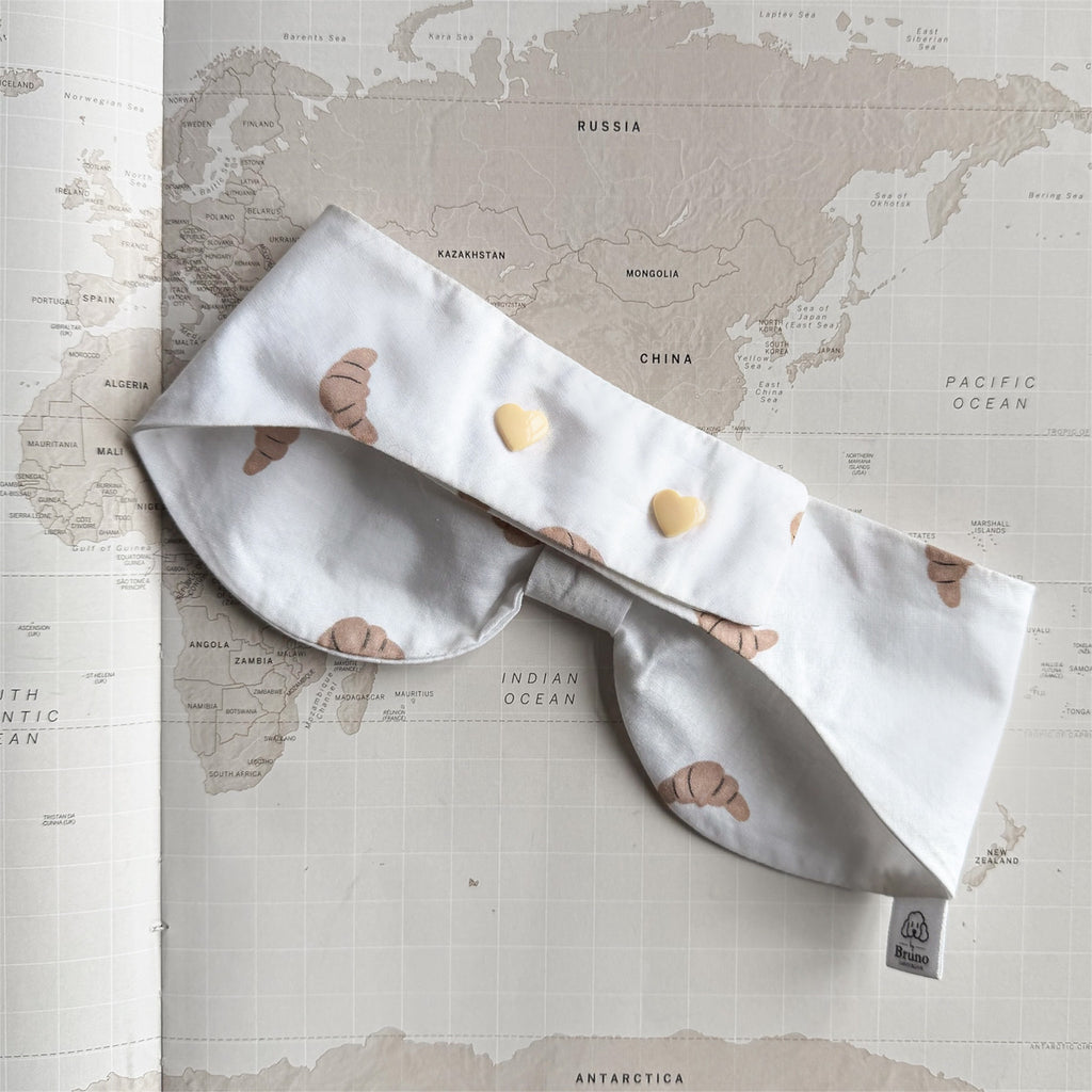 Back side of the white bowdana with brown croissants and beige buttons on a world map background.