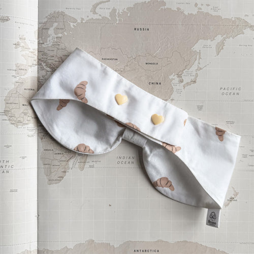 Back side of the white bowdana with brown croissants and beige buttons on a world map background.