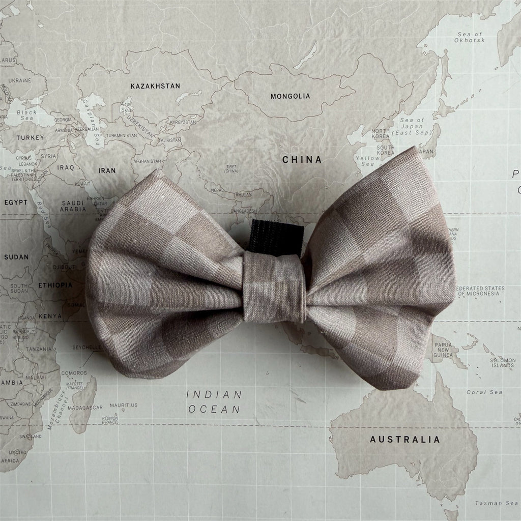 A dog bow tie with a muted taupe and beige checkered pattern, laid flat on a vintage-style world map background.