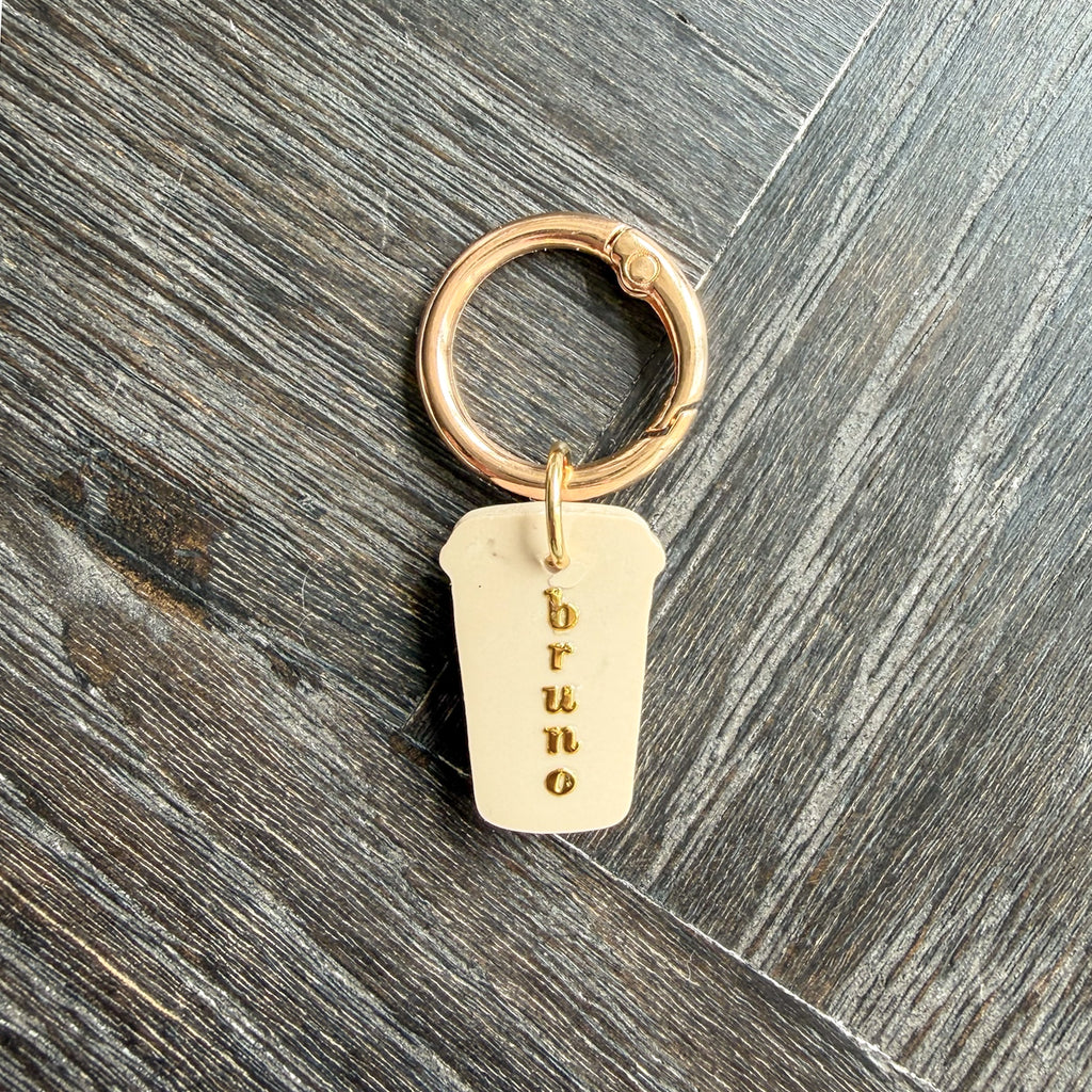 Back side of the green coffee cup dog tag with a dog's name in gold letters on a world map background.