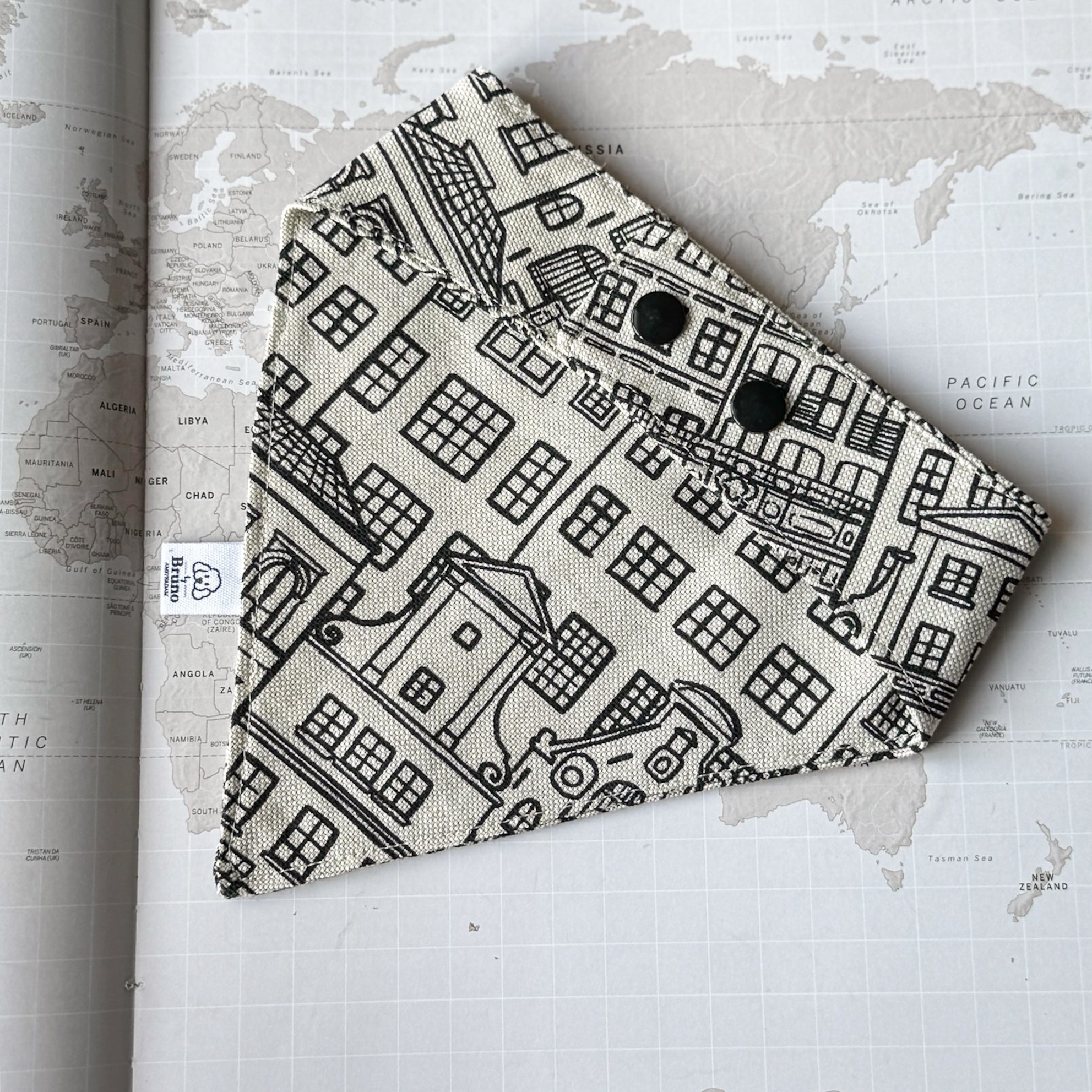 A back side of a dog bandana with Amsterdam Canal Houses print and black plastic buttons on a world map background.