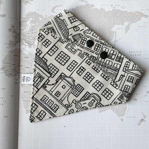 A back side of a dog bandana with Amsterdam Canal Houses print and black plastic buttons on a world map background.