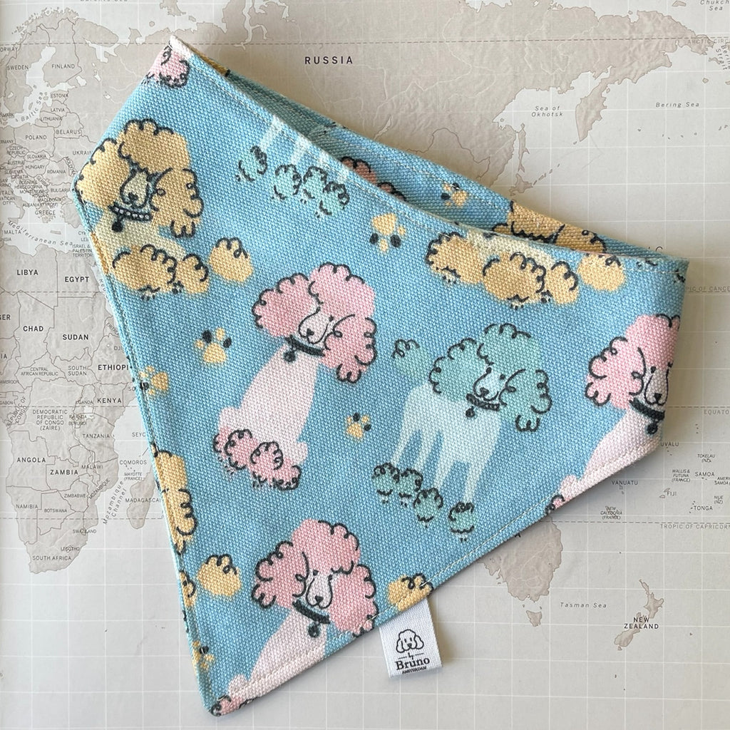 A blue dog bandana with multicolored poodles on a world map background.