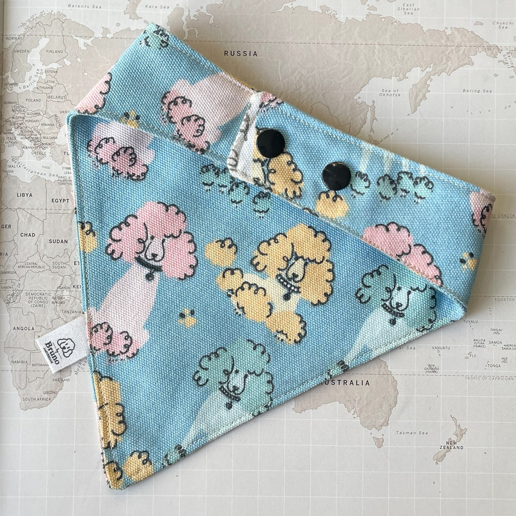 Back side of a blue dog bandana with multicolored poodles and two black plastic buttons on a world map background.