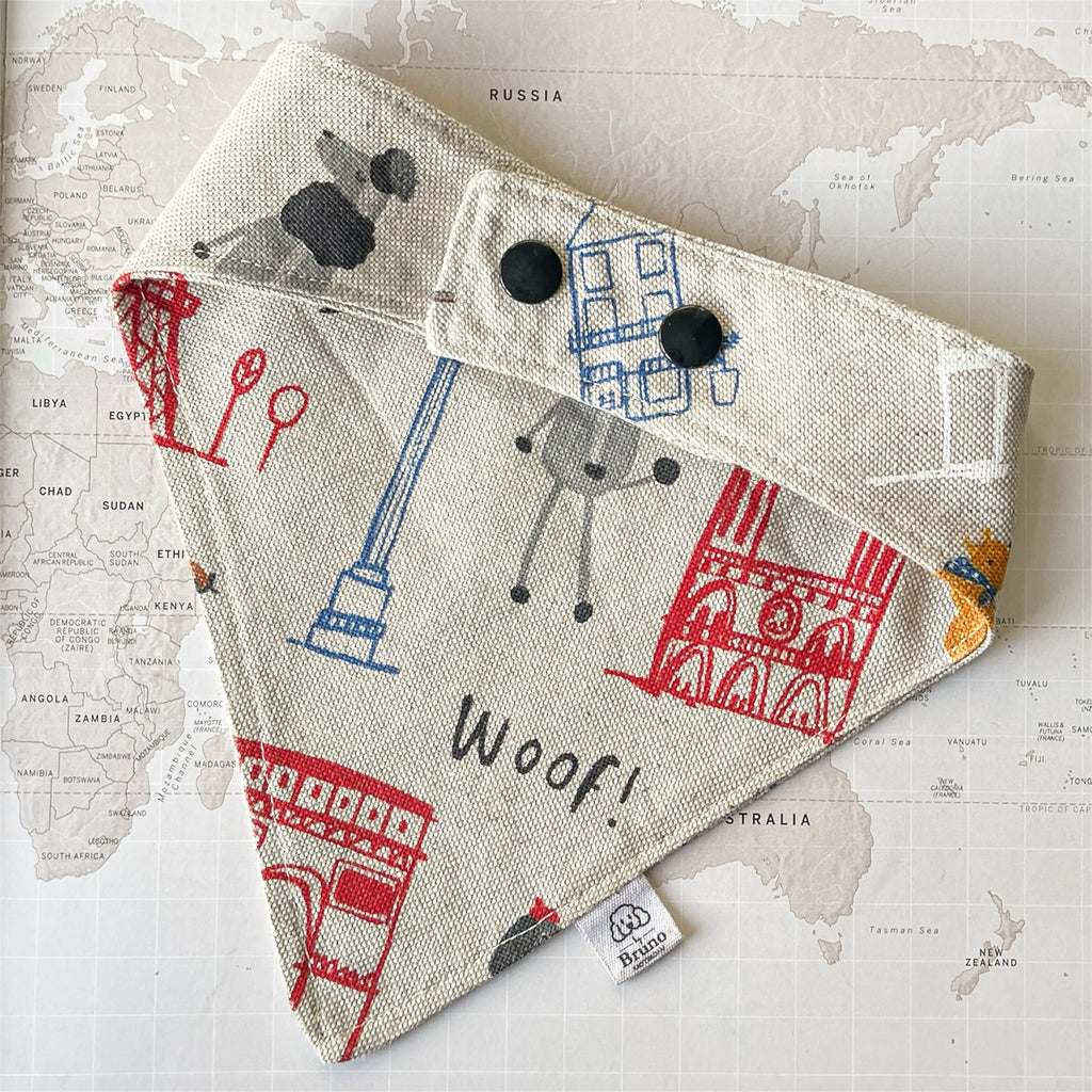 Back side of a dog bandana with Paris motifs and two black plastic buttons on a world map background.