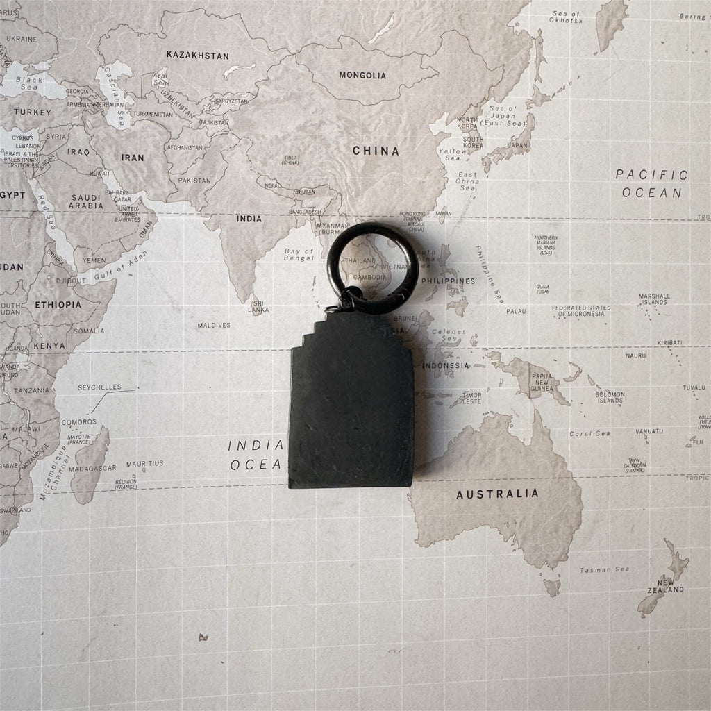 Back side of the Amsterdam house shaped dog tag on a world map surface.