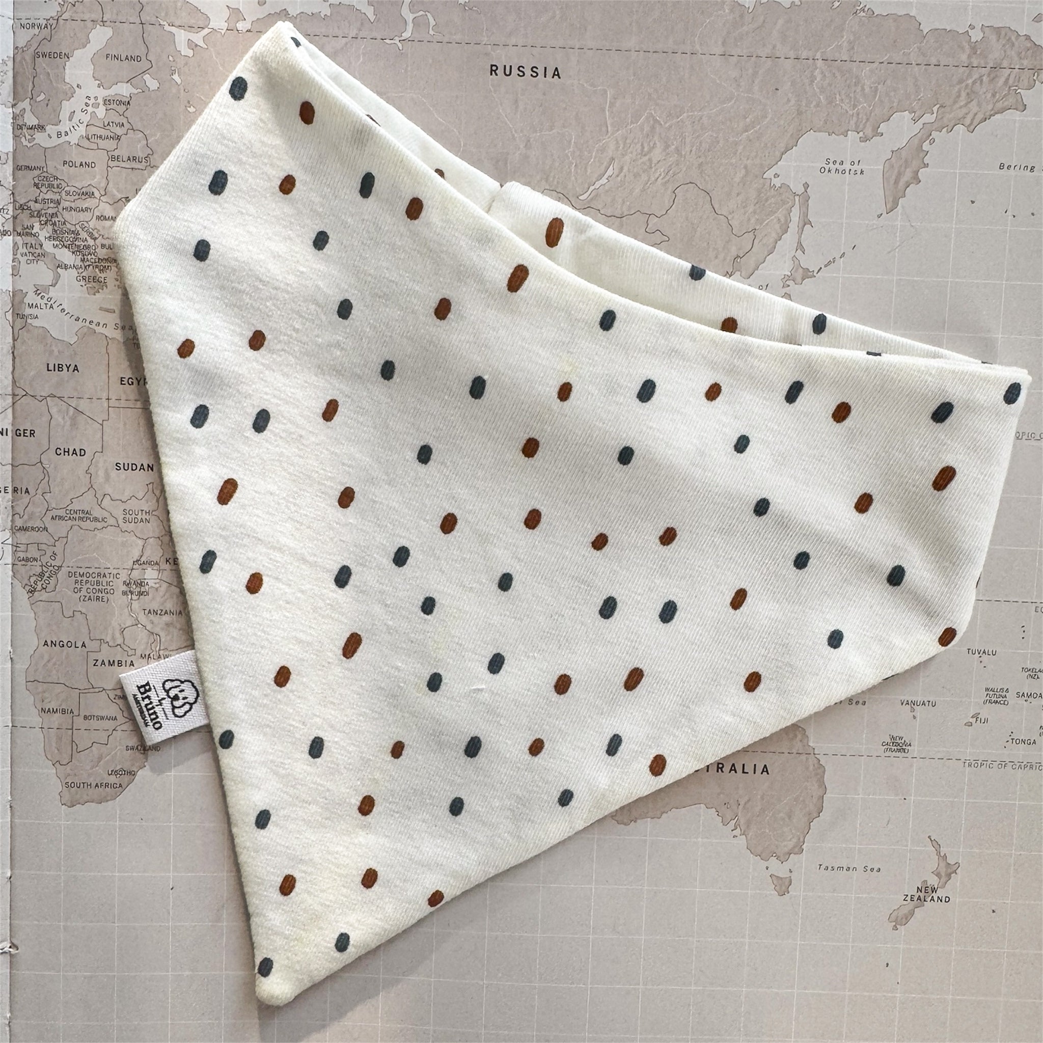 White dog bandana with blue and rusted dots on a world map background.