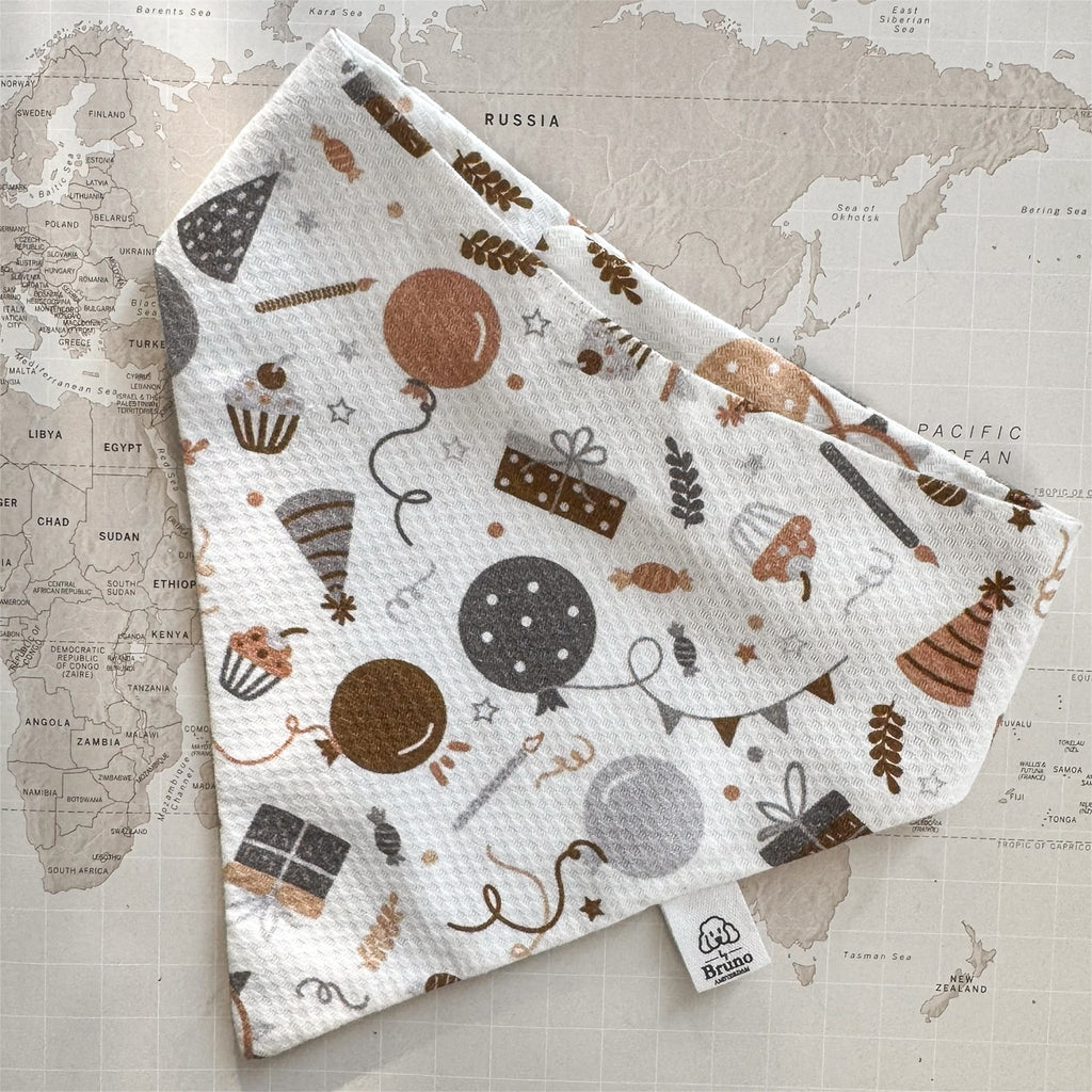 White dog bandana with balloons, wrapped gifts, cupcakes and party hats on a world map background.