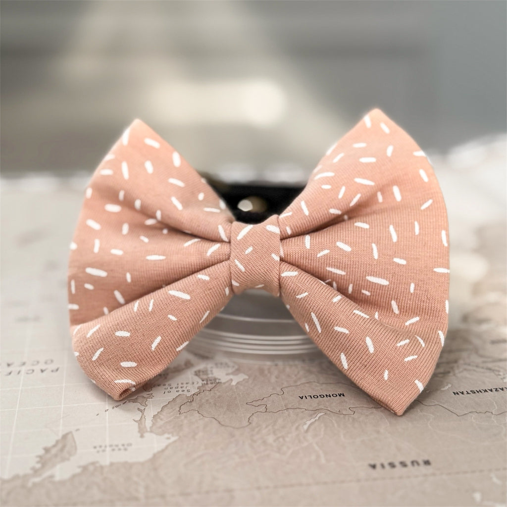 Warm apricot dog bow with white sprinkle print on a world map background.