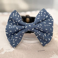 Dusty blue dog bow with white sprinkle print on a world map background.