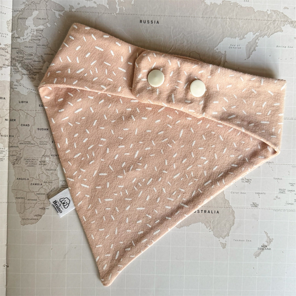 Back side of the warm apricot dog bandana with a soft, tonal scattered pattern on a world map background, closed with pearl coloured buttons.
