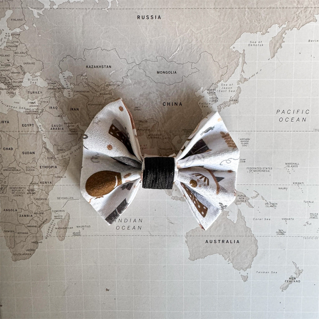 White dog bow with birthday print and an elastic loop on a world map surface.