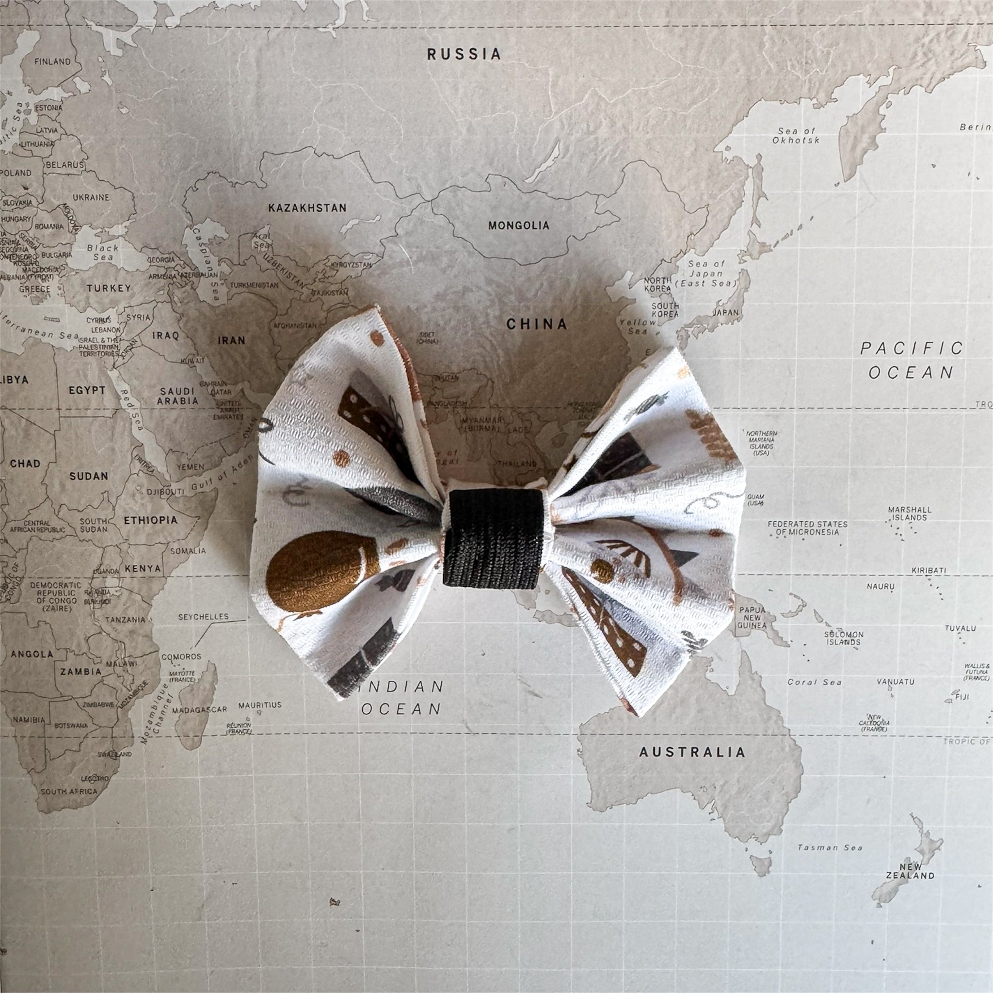 White dog bow with birthday print and an elastic loop on a world map surface.