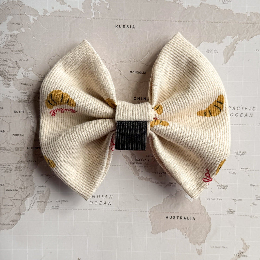 Back side of the dog bow with brown croissants and red words in French with an elastic loop.
