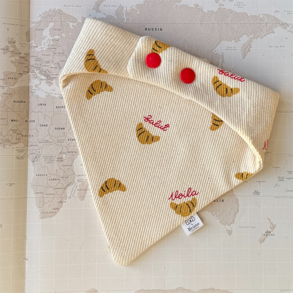 Back side of the dog bandana with croissants and French words in red, closing with red buttons.