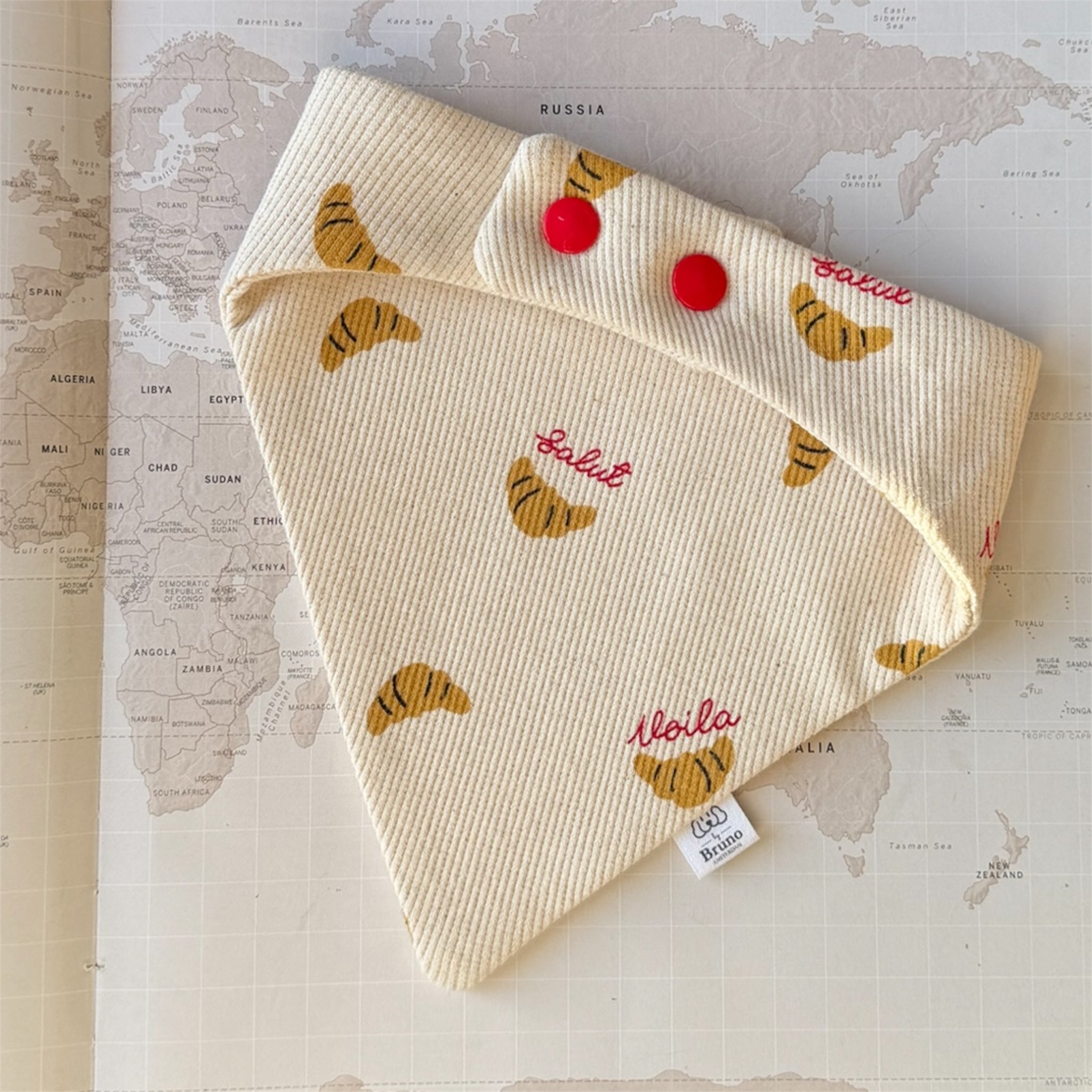 Back side of the dog bandana with croissants and French words in red, closing with red buttons.