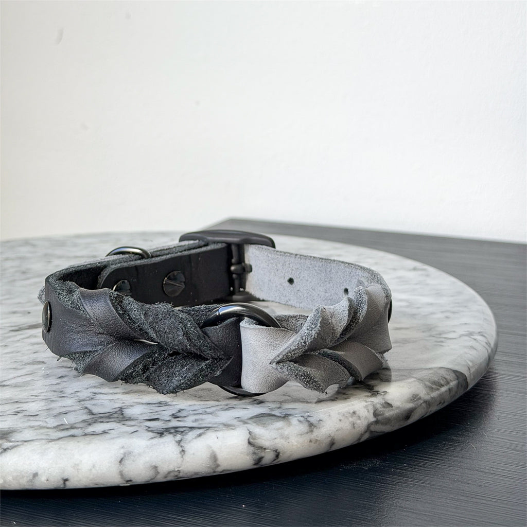 Handmade grey leather dog collar with braided detail and metal hardware on a marble surface.