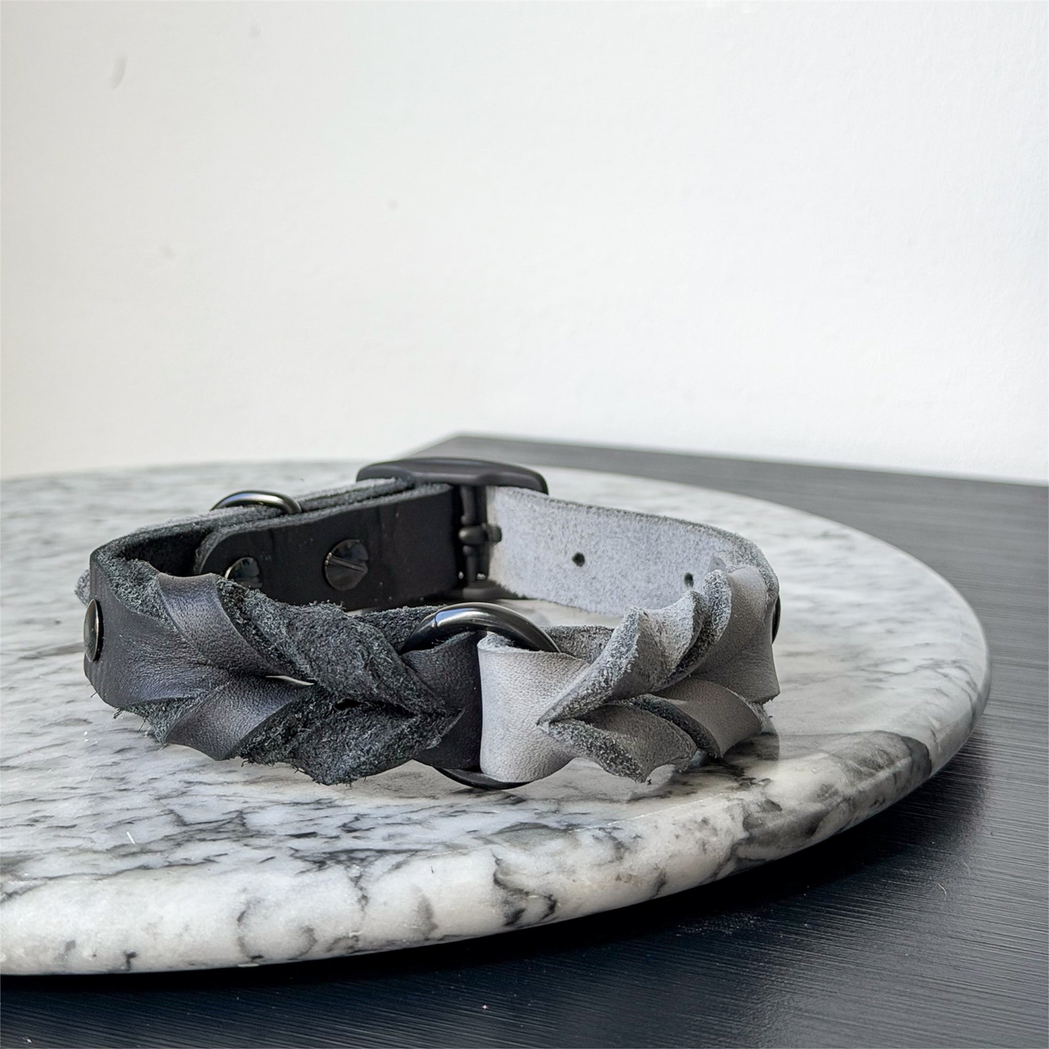 Handmade grey leather dog collar with braided detail and metal hardware on a marble surface.