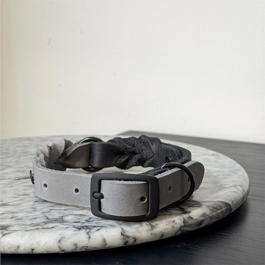 Handmade grey leather dog collar with braided detail and metal hardware on a marble surface.
