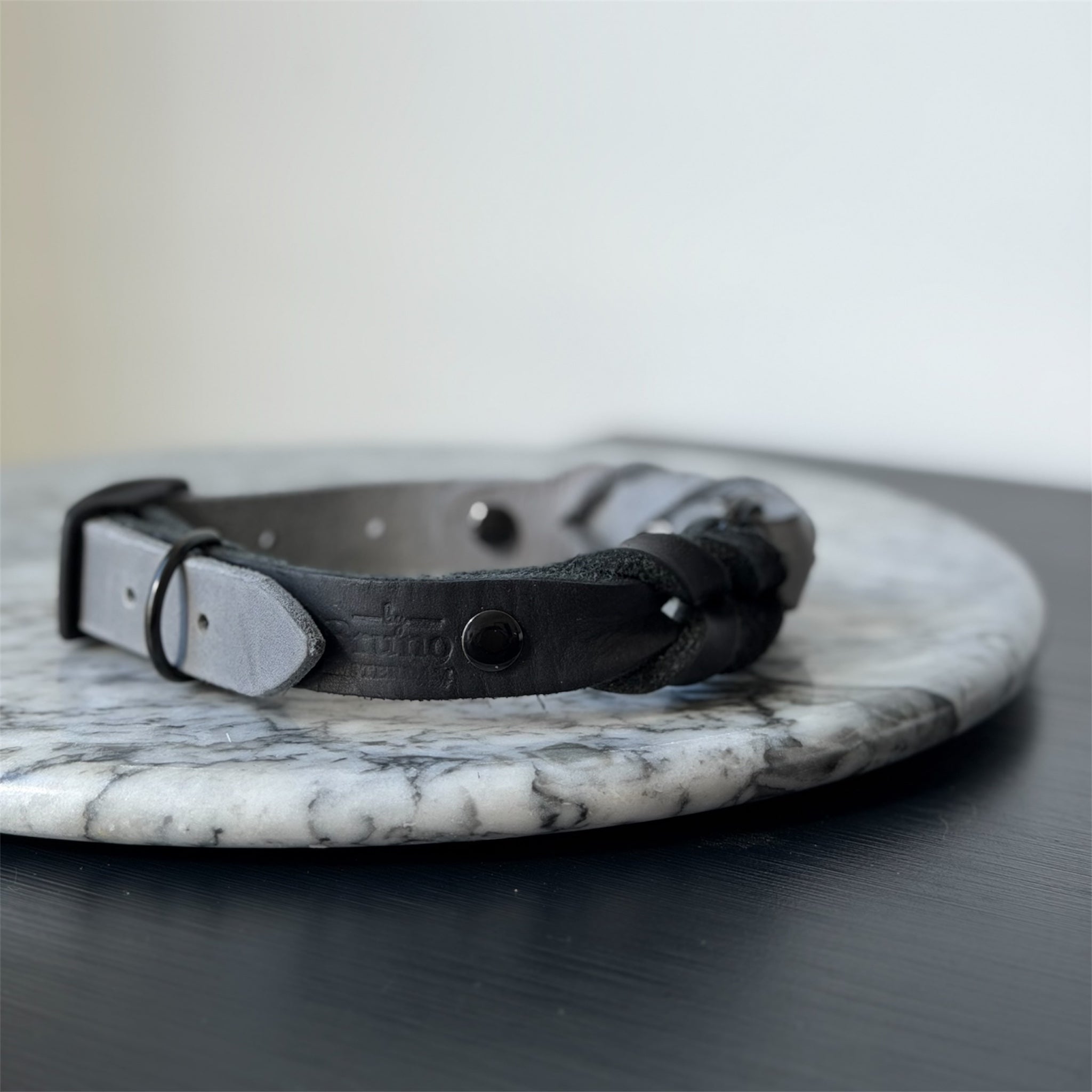 Handmade grey leather dog collar with braided detail and metal hardware on a marble surface.