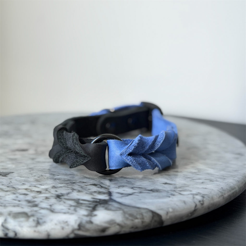 Handmade blue leather dog collar with braided detail and metal hardware on a marble surface.