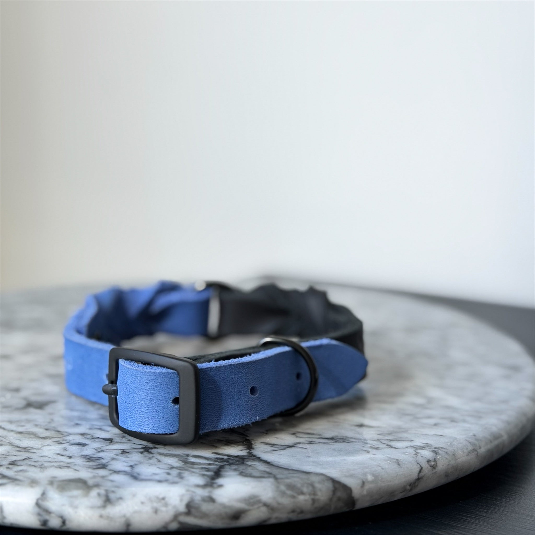 Handmade blue leather dog collar with braided detail and metal hardware on a marble surface.