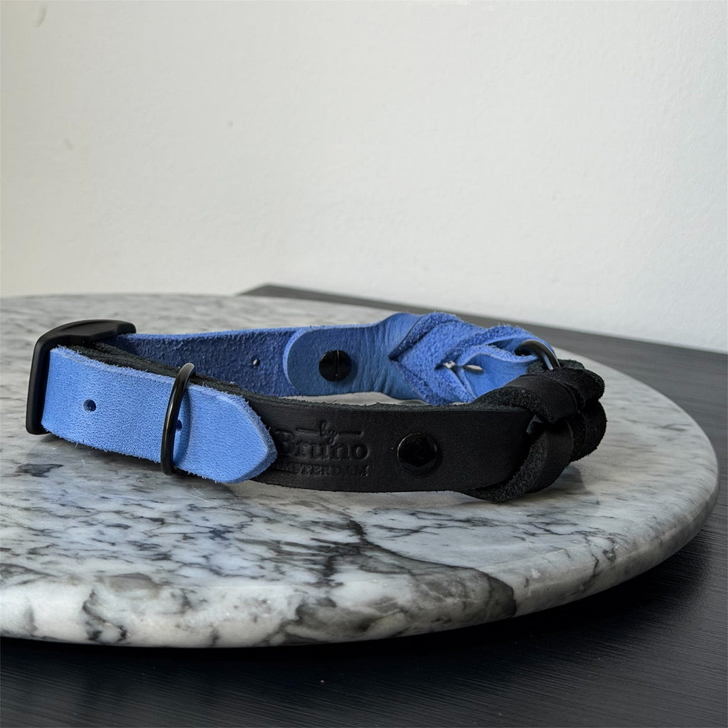 Handmade blue leather dog collar with braided detail and metal hardware on a marble surface.