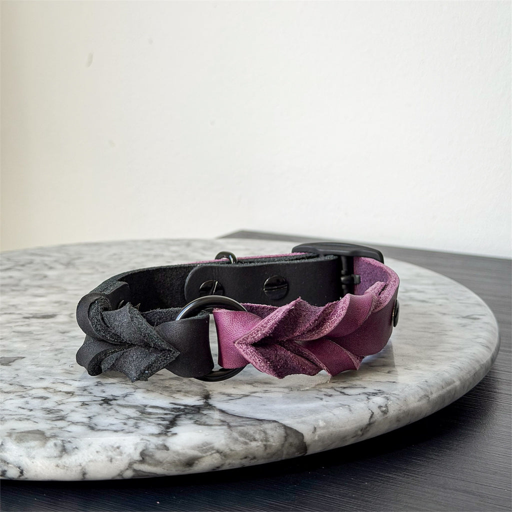 Handmade purple and black leather dog collar with black metal hardware on a marble surface.