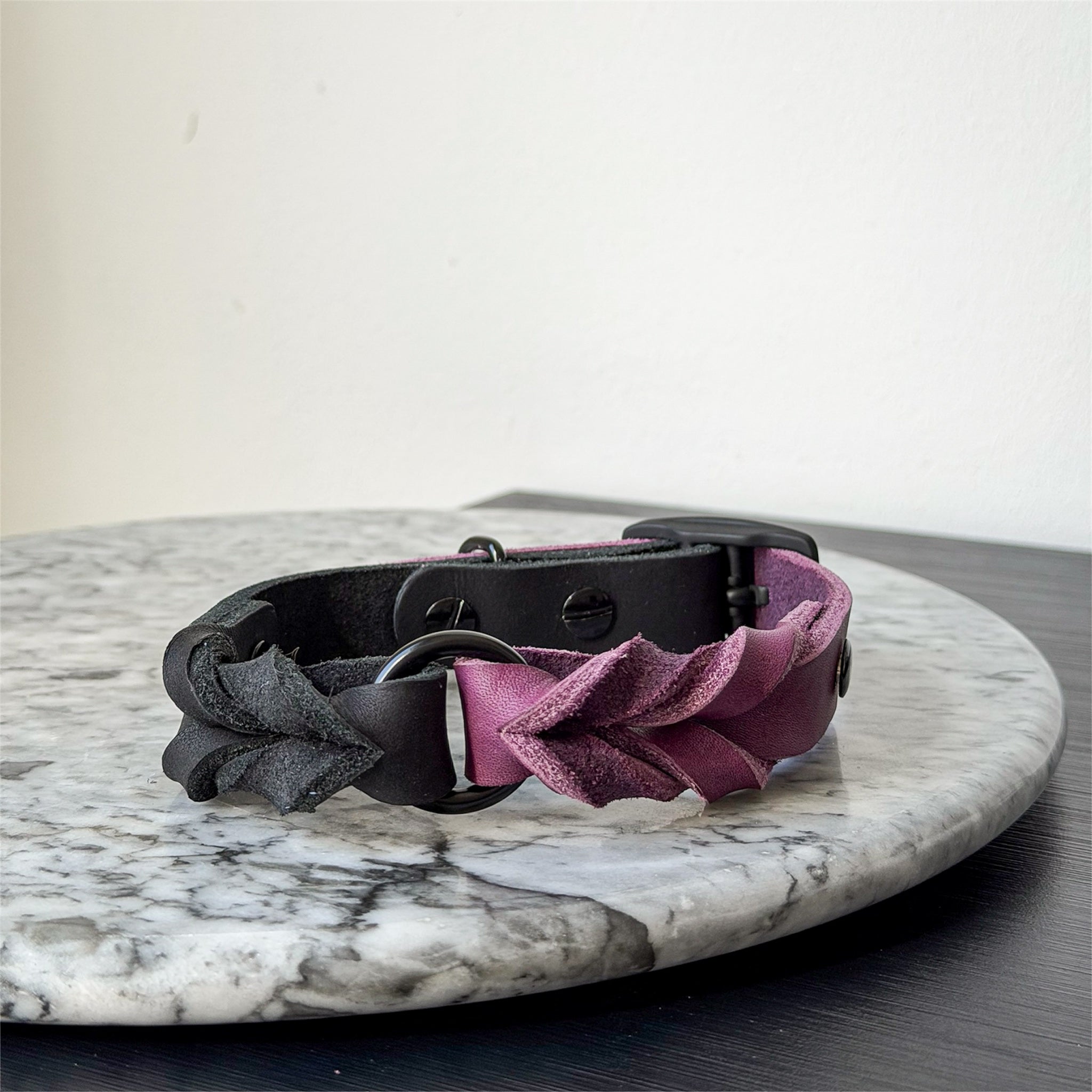 Handmade purple and black leather dog collar with black metal hardware on a marble surface.