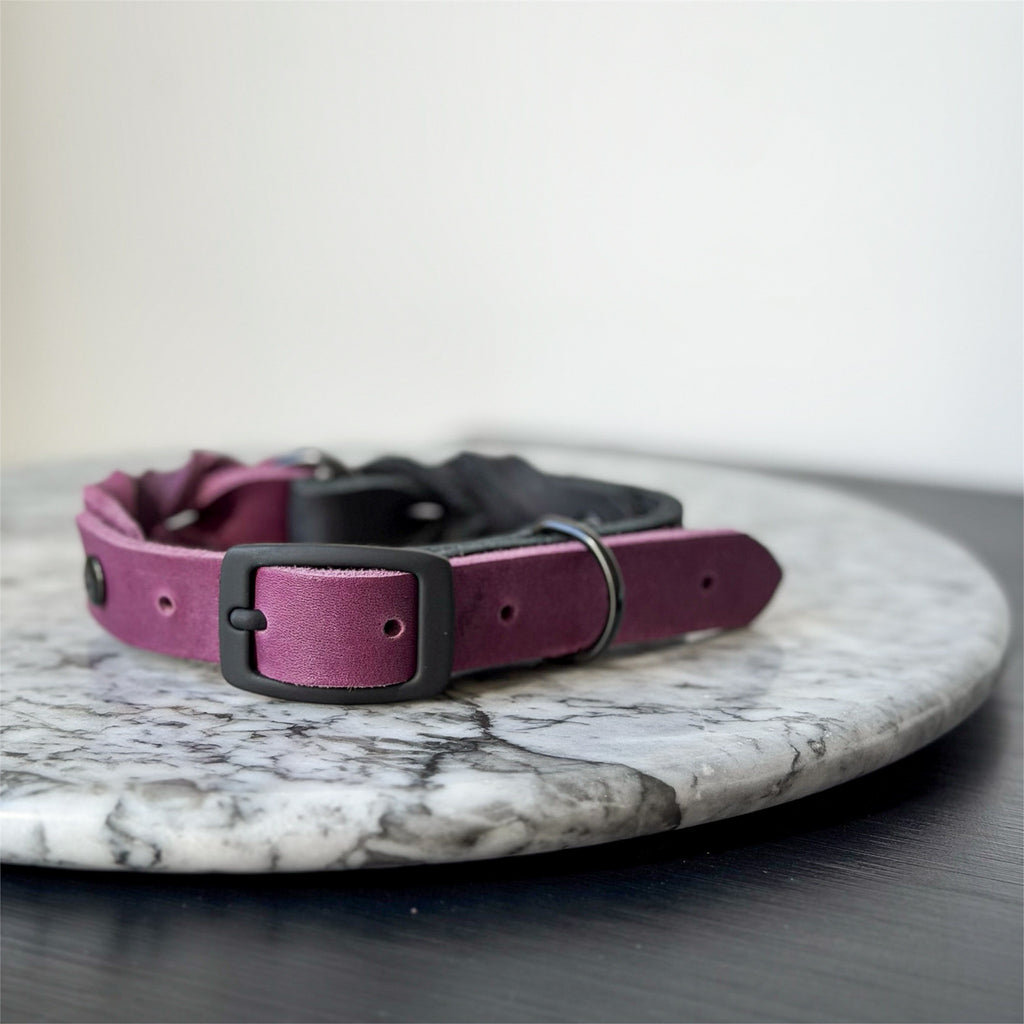 Handmade purple and black leather dog collar with black metal hardware on a marble surface.