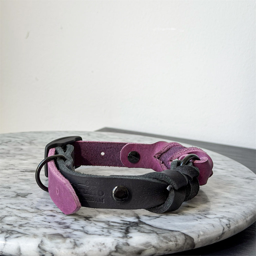 Handmade purple and black leather dog collar with black metal hardware on a marble surface.