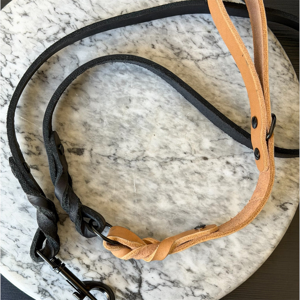 Camel leather dog leash with black hardware on a marble surface.