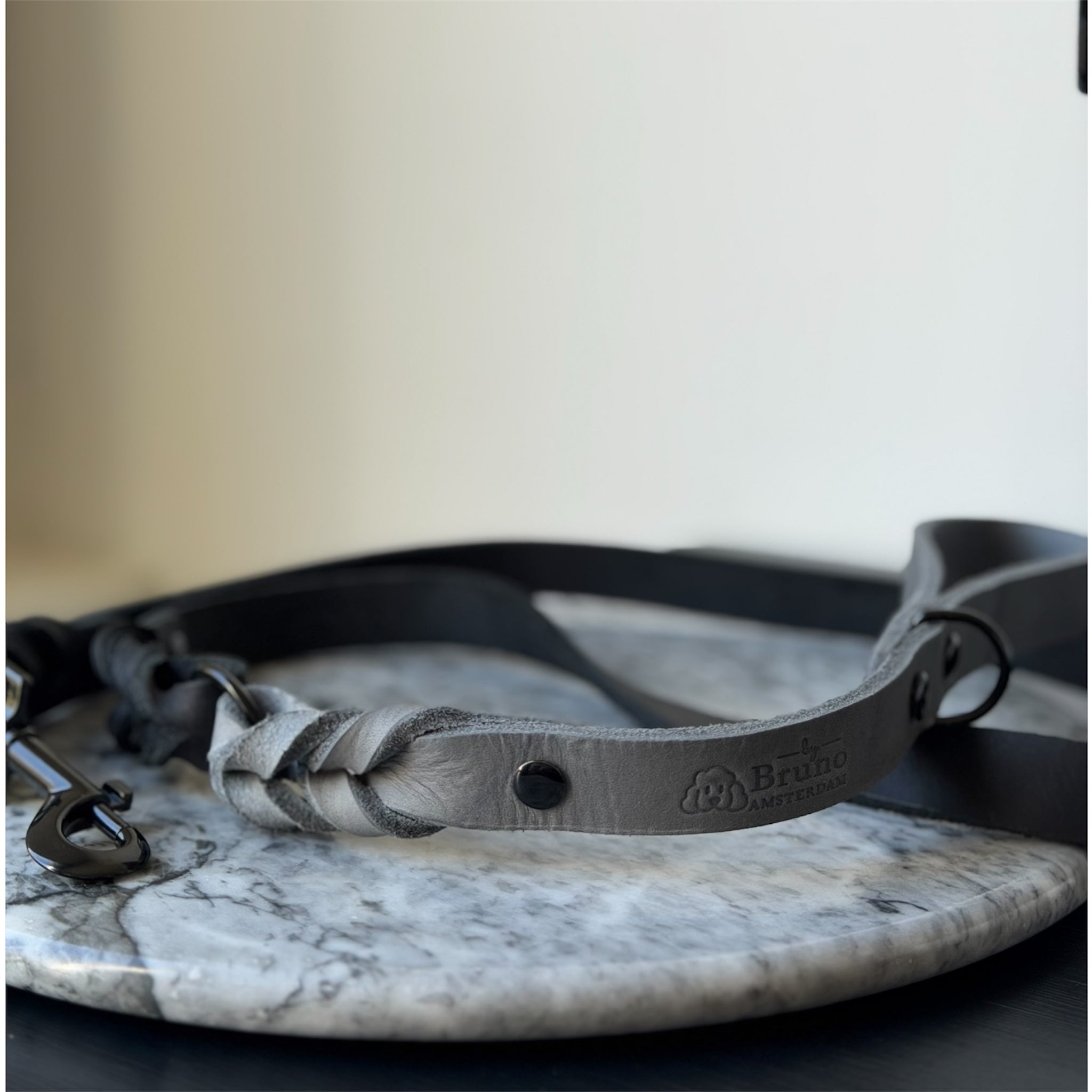 Grey leather braided dog leash with black hardware on a marble surface.