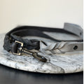 Grey leather braided dog leash with black hardware on a marble surface.