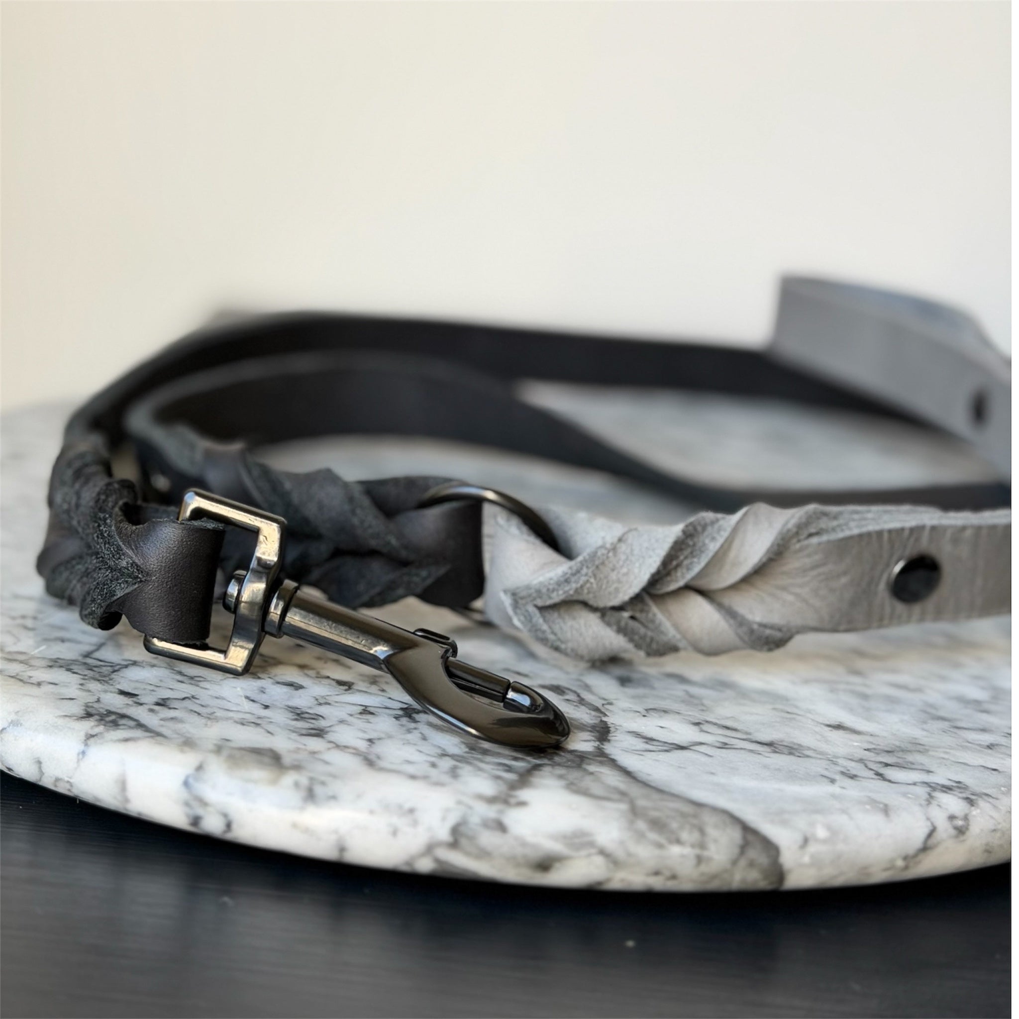 Grey leather braided dog leash with black hardware on a marble surface.
