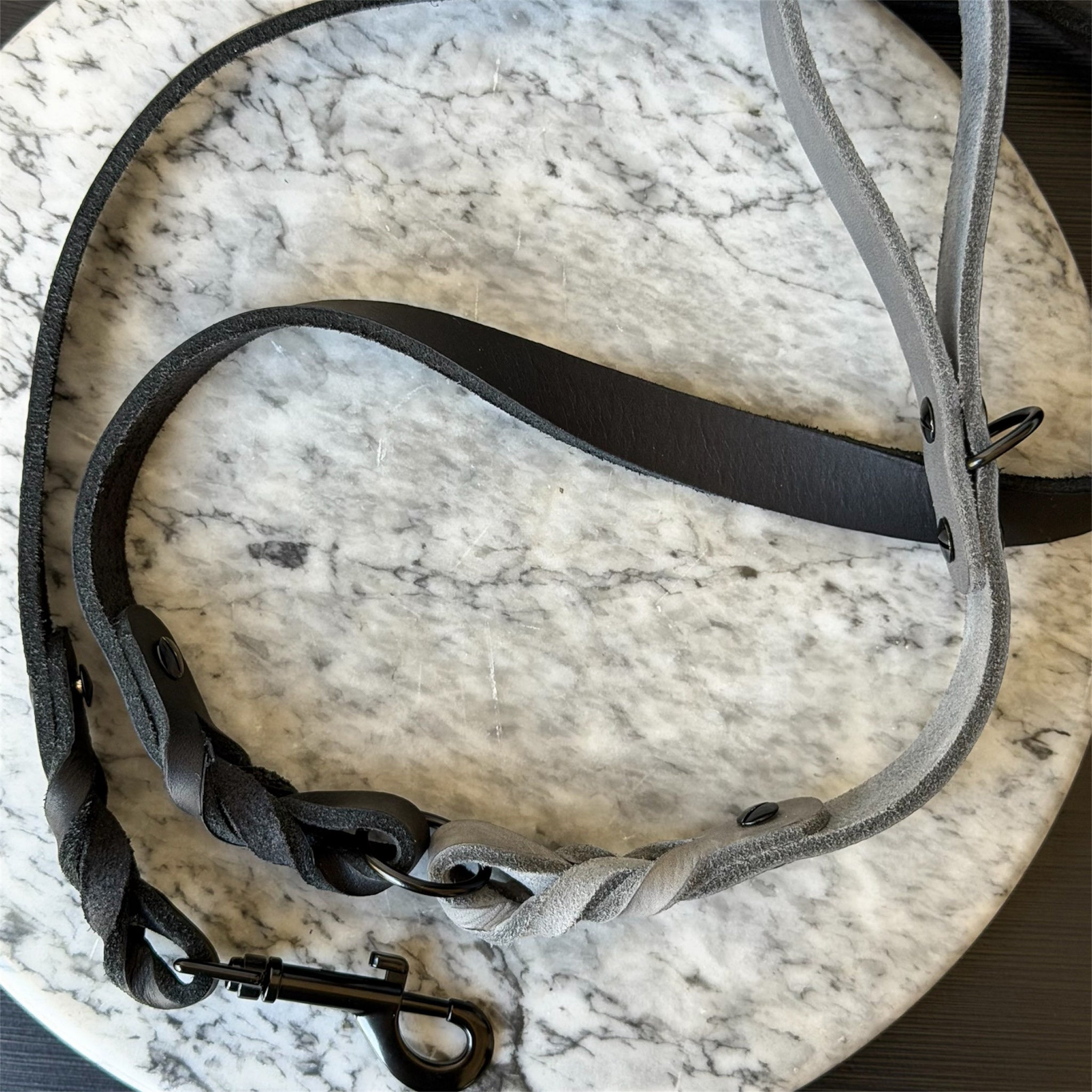 Grey leather braided dog leash with black hardware on a marble surface.