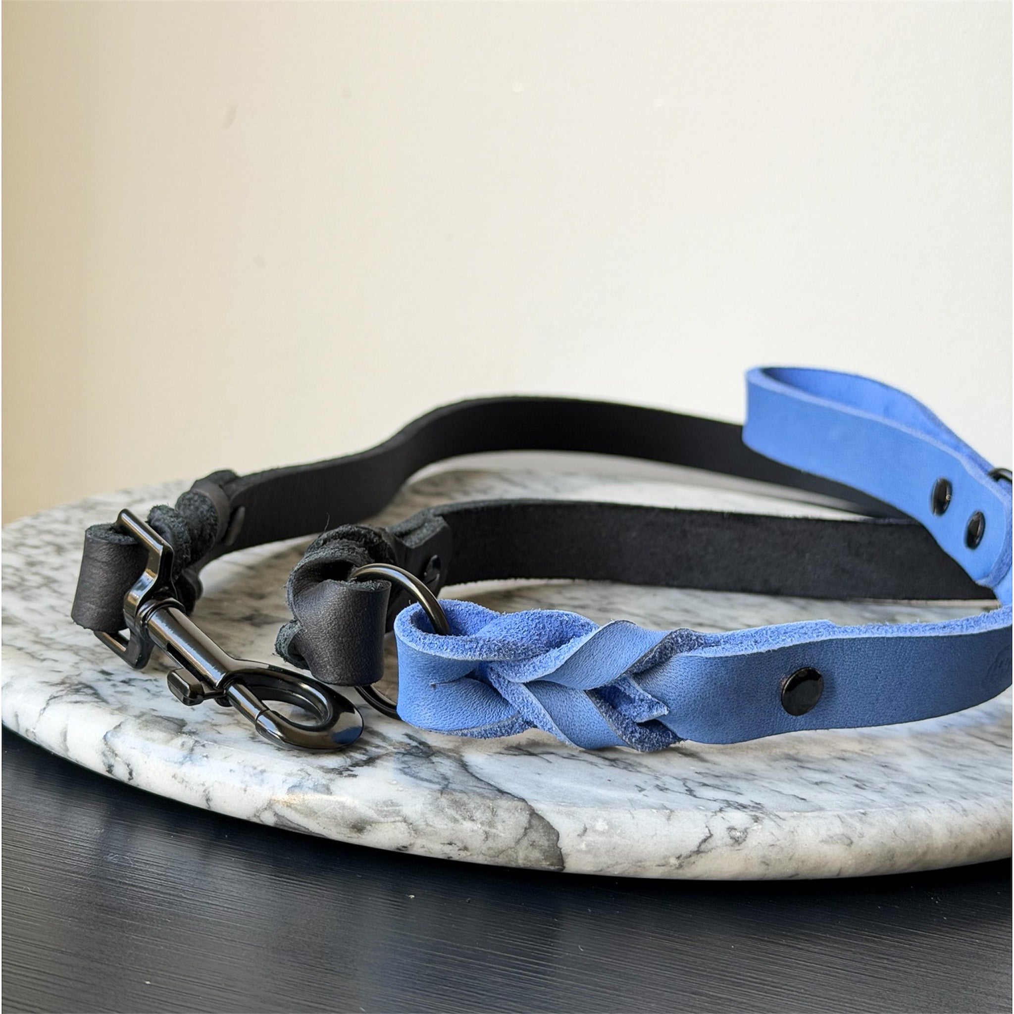 Blue and black leather dog leash with a metal clasp on a marble surface.