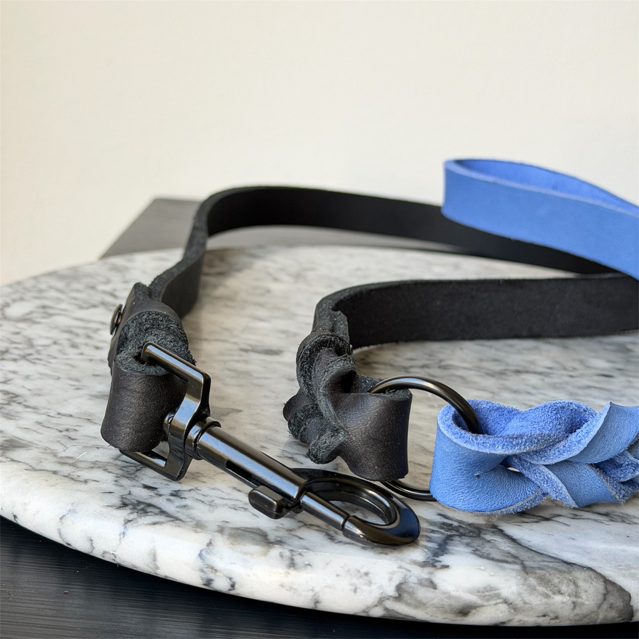 Blue and black leather dog leash with a metal clasp on a marble surface.