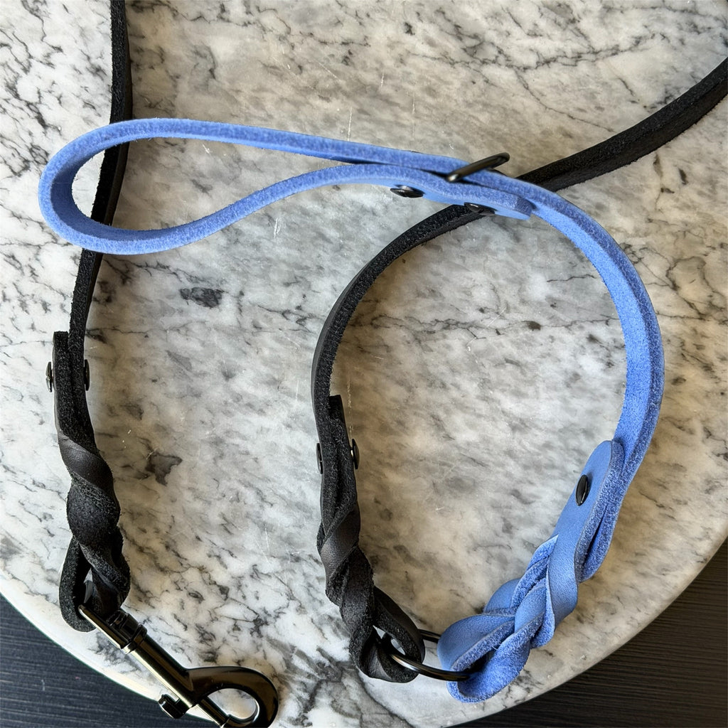 Blue and black leather dog leash with a metal clasp on a marble surface.