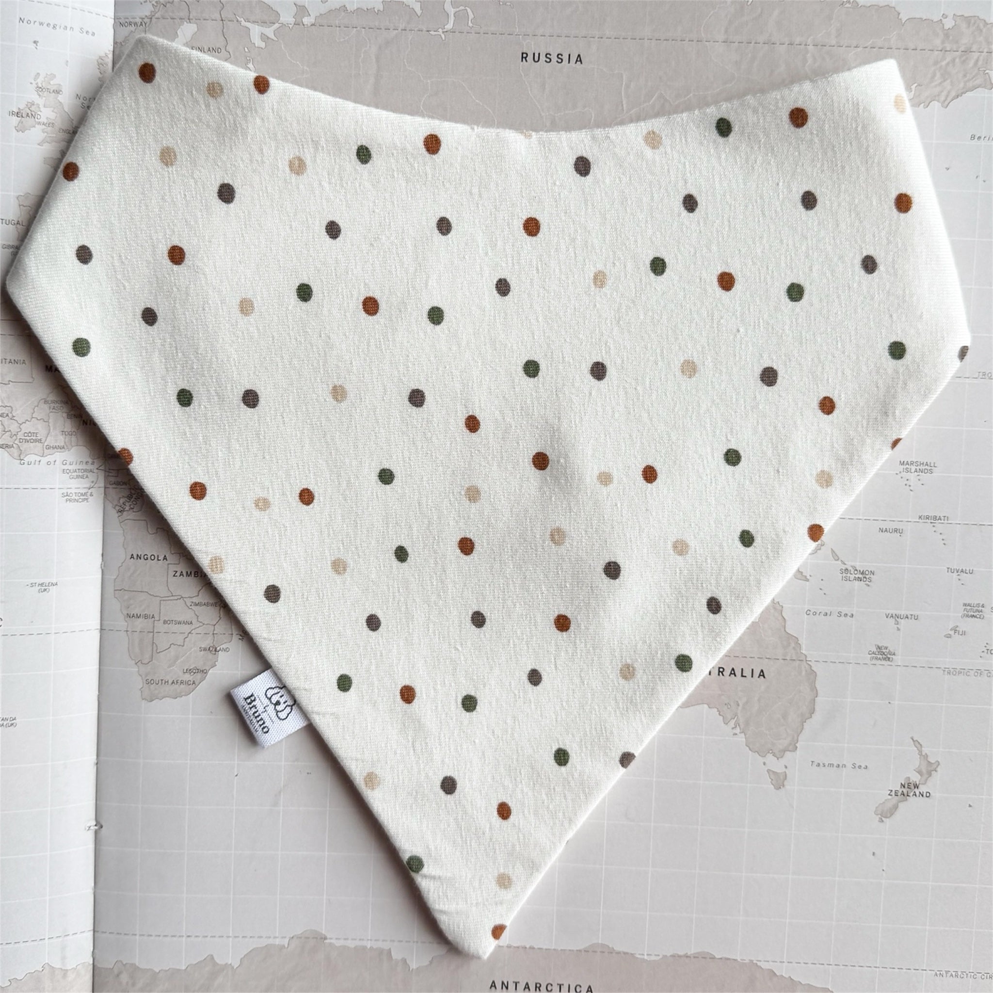 White dog bandana with green and rusted dots on a world map background.