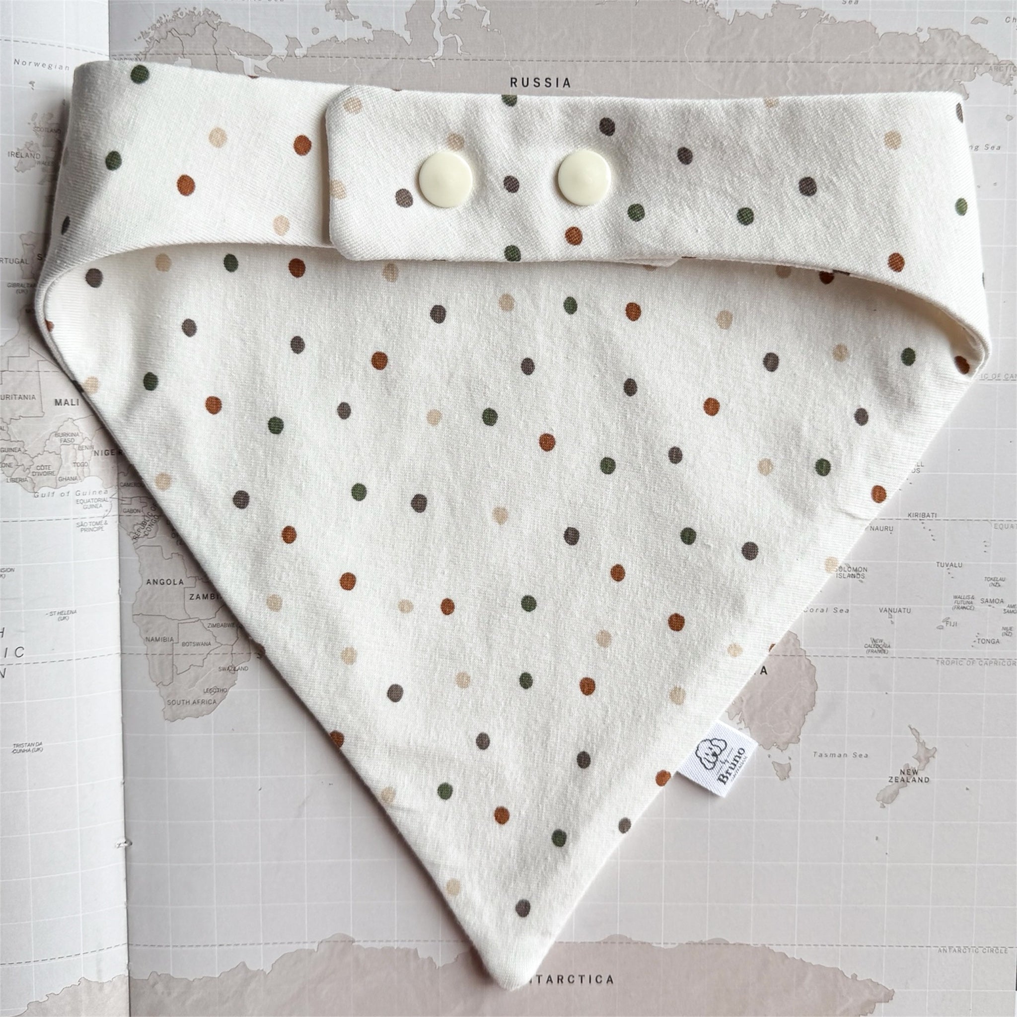 Back side of the white dog bandana with plastic pearl coloured buttons on a world map background.