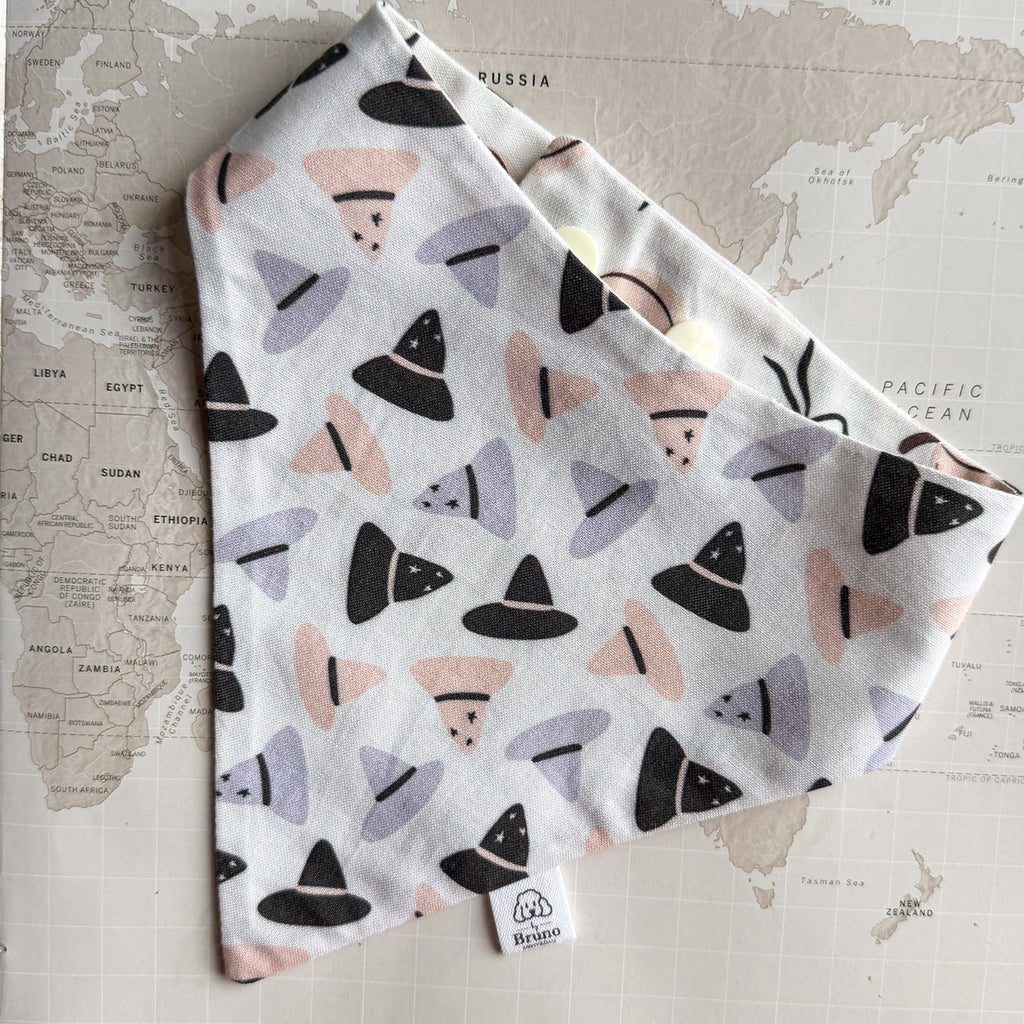 White cotton dog bandana with orange, purple and black witch hats on a world map background.