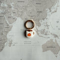 A coffee mug dog tag with an orange pumpkin design, attached to a gold split ring, displayed on a vintage-style world map background.