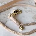 A close-up of a beige braided rope leash with a gold-tone metal clasp, resting on a vintage-style world map background.