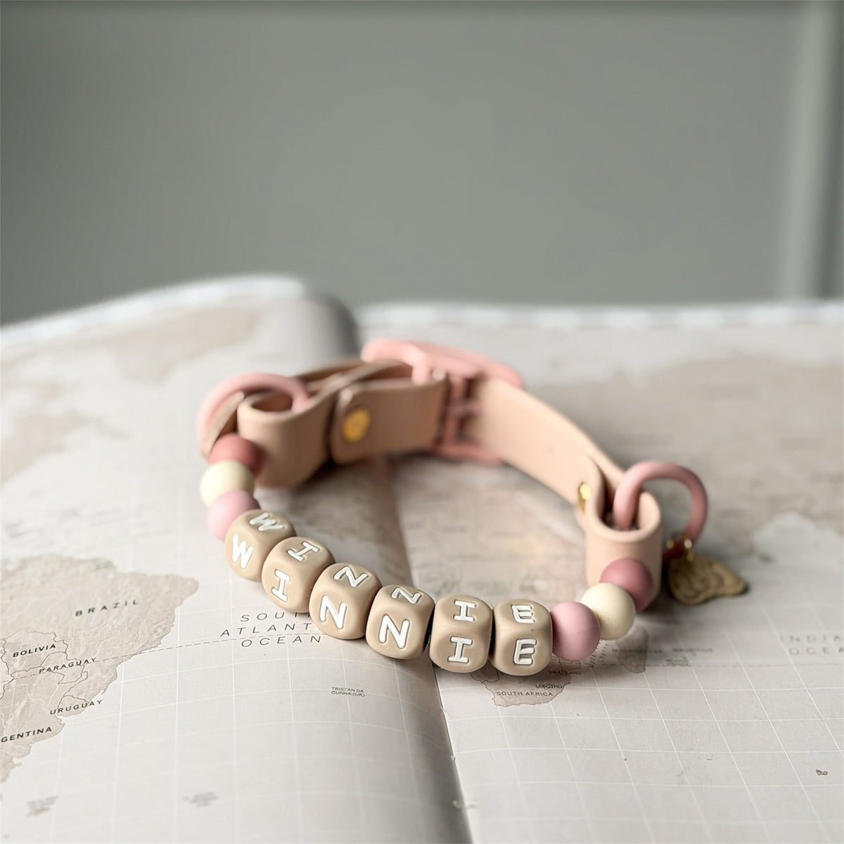 Personalised dog collar with silicone beads indue and pink tones on a world map background.