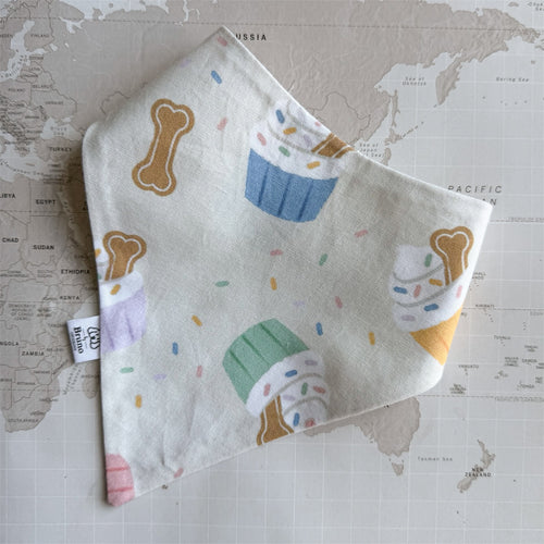 Handmade Birthday Party dog bandana featuring cupcakes, dog biscuits and colourful sprinkles, photographed on a vintage world map.