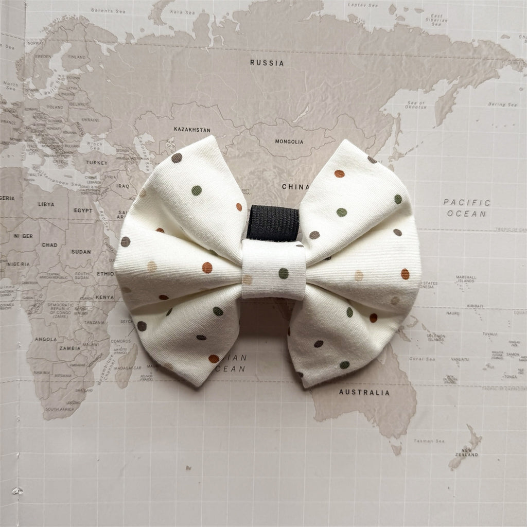 White dog bow with brown and green polka dots on a world map background.