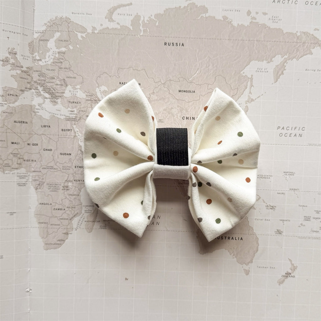 Back of the white dog bow with brown and green polka dots and elastic loop on a world map background.